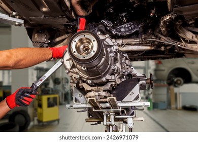 A car raised on a lift for repair and under it a detached Transmission gearbox suspended on a crane and a gear box on a lifting in a vehicle repair shop with view to the bottom . - Powered by Shutterstock