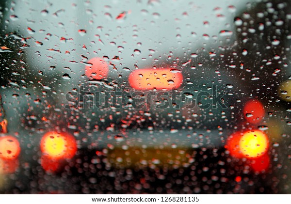 Car rear brake lights reflecting on raindrops\
of car windscreen.