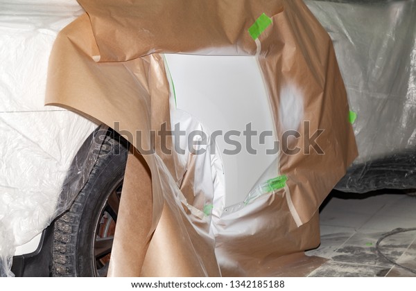 The car rear\
view after the accident in the camera for car body repair is\
partially covered with paper and pasted over with green masking\
tape for painting the side door with\
white