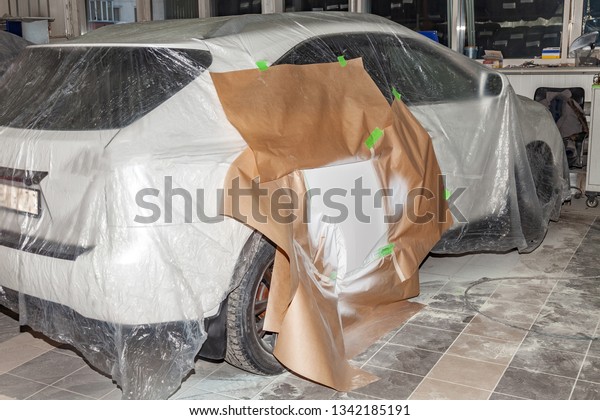 The car rear\
view after the accident in the camera for car body repair is\
partially covered with paper and pasted over with green masking\
tape for painting the side door with\
white