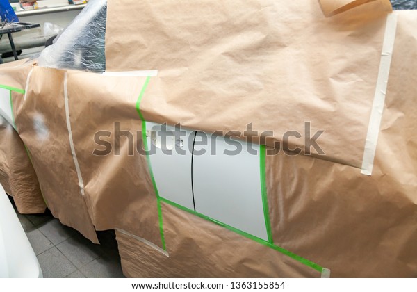 The car rear\
view after the accident in the camera for car body repair is\
partially covered with paper and pasted over with green masking\
tape for painting the side doors with\
white