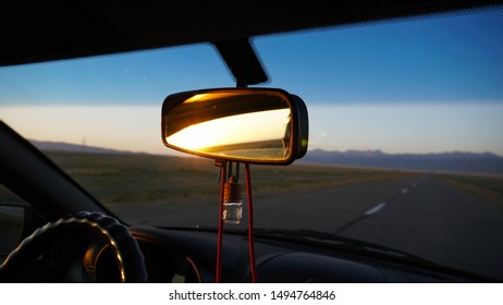 Car Rear View Mirror. Displays Orange Dawn. Visible Road, Hills And Steppe. Hang Key Chains. The Car Goes Fast. Kazakhstan Road, Near Almaty.