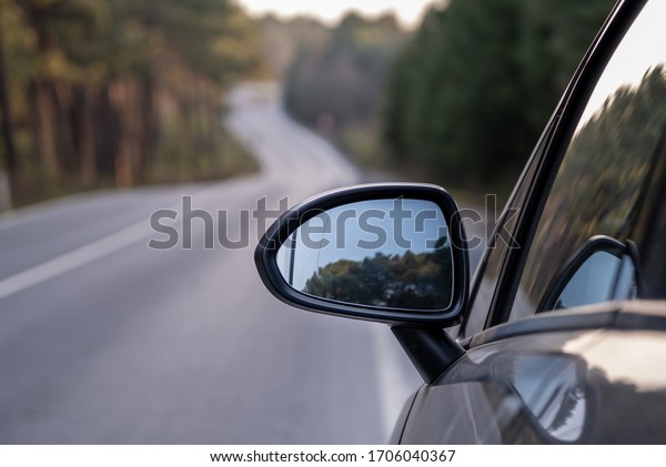 Car rear view\
mirror on wooded rural road