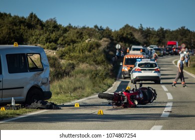 Car And A Red Sport Motorcycle Crash Scene On An Open Road In Afternoon. Workers And Police Seen Around The Crash Site, With A Queue Of Traffic Building Behind. Destroyed Van And Motorcycle.