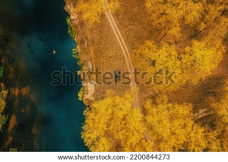 Car Renault Duster SUV parked near river landscape. Aerial view of yellow forest woods and river in autumn landscape. Top view of beautiful european nature from high attitude in autumn season. Bird's
