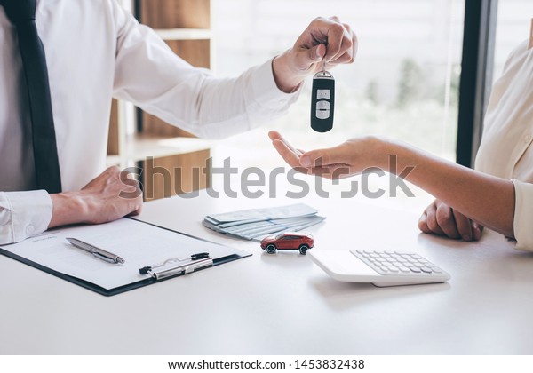 Car rent agent manager holding key of new car\
giving to woman client after signing good deal agreement contract,\
renting considering\
vehicle.
