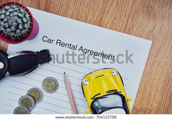 Car rental agreement paper with key, coins and car\
model on wooden table