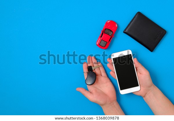 Car rental app concept. Toy car,\
auto drive license, human hands holding smartphone and car car key\
on blue background. Flat lay composition. Top\
view.
