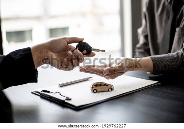 A car rental company employee is handing out the\
car keys to the renter after discussing the rental details and\
conditions together with the renter signing a car rental agreement.\
Concept car rental.