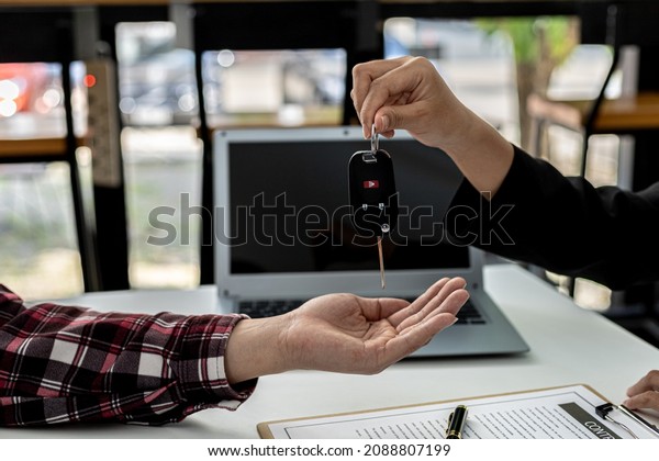 A car rental company employee is handing out the\
car keys to the renter after discussing the rental details and\
conditions together with the renter signing a car rental agreement.\
Concept car rental.