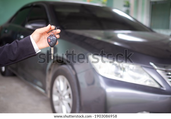 Car rental driver.hand woman holding car keys on\
blur image of black car. for buying or selling a car. business or\
finance concept.