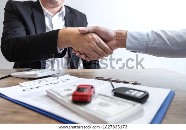 Car rental and Insurance concept, Young\
salesman shaking hands after finishing up a collaboration\
discussing with customer after sign agreement contract with\
approved good deal for rent or\
purchase.
