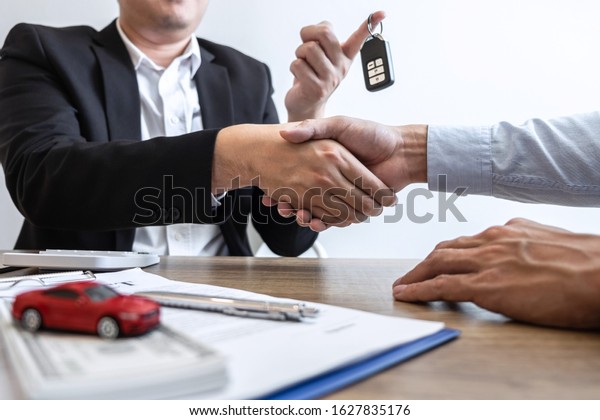 Car rental and Insurance concept, Young\
salesman shaking hands after finishing up a collaboration\
discussing with customer after sign agreement contract with\
approved good deal for rent or\
purchase.
