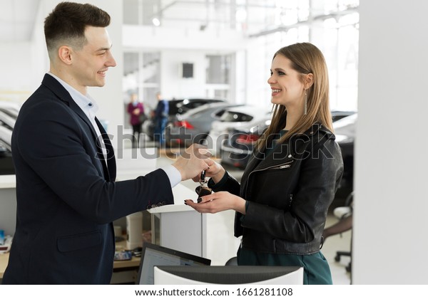 Car rental and\
Insurance concept, Young salesman receiving money and giving car\'s\
key to customer after sign agreement contract with approved good\
deal for rent or purchase.