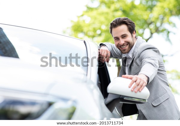 Car rental or purchase in showroom, cheerful facial\
expression, young man chooses new automobile at car dealership.\
Attractive satisfied european man in suit touching new transport in\
auto store