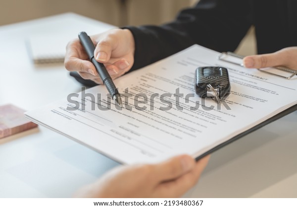 Car rental\
service concept. Close up view Hand of agent giving car key to\
customer after signed rental contract\
form.