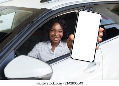 Car Renting App. Happy Black Female Showing Blank Smartphone While Sitting Inside Of Auto, Smiling African American Woman Demonstrating Copy Space For Mobile Advertisement Or Website, Mockup