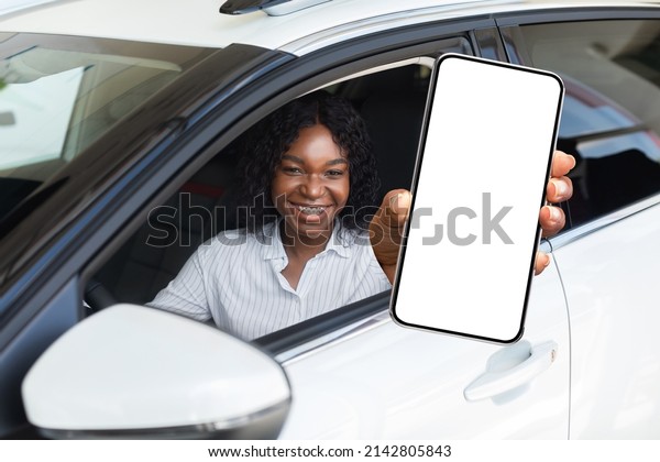 Car Renting App. Happy Black Female Showing Blank\
Smartphone While Sitting Inside Of Auto, Smiling African American\
Woman Demonstrating Copy Space For Mobile Advertisement Or Website,\
Mockup