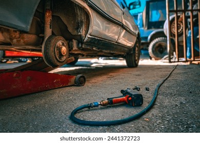 Car repair in action: A white car lifted by a jack, tire removed for maintenance, pneumatic nut runner, showcasing real-life auto repair services. - Powered by Shutterstock