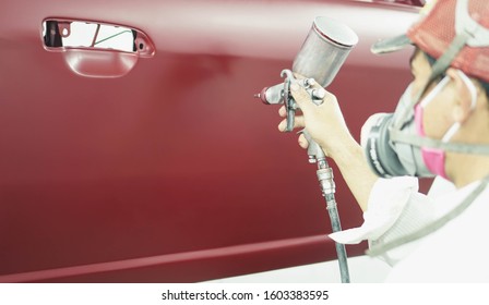 Car Repair auto mechanic worker painting a car in with airbrush pulverizer painting car body in paint chamber