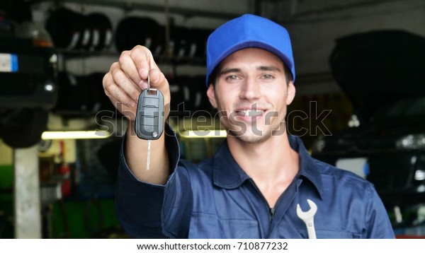 In a car repair garage a mechanic after settling\
the car shows the keys as a car\'s ready to start. Concept of:\
security, safety, insurance, keys of the future, assistance and\
customer care.