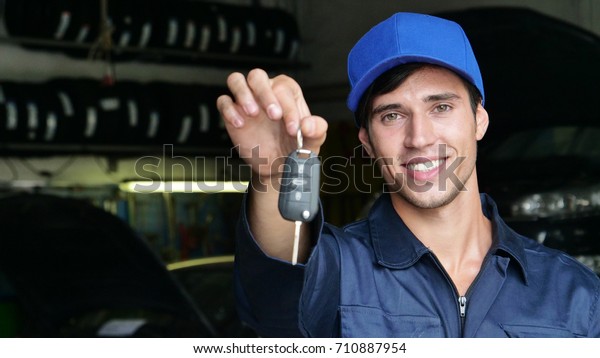 In a car repair garage a mechanic after settling\
the car shows the keys as a car\'s ready to start. Concept of:\
security, safety, insurance, keys of the future, assistance and\
customer care.