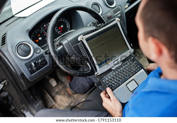 Car repair and maintenance theme. Electric\
mechanic in uniform working in auto service, making car diagnostics\
using obd device with laptop.\
