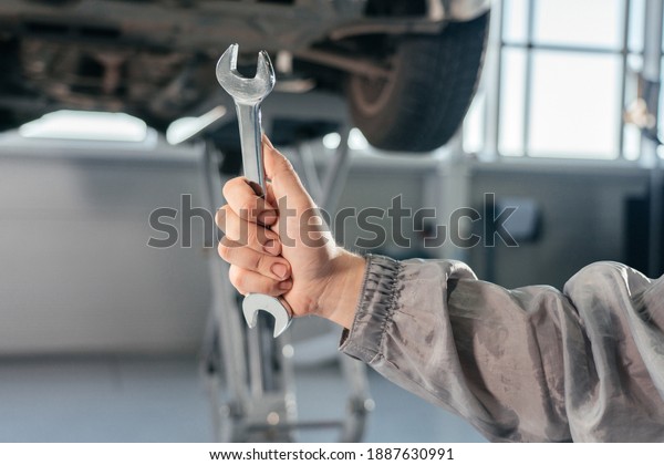 Car repair, maintenance and\
vehicle inspection concept. Man holding wrench in front of a\
car