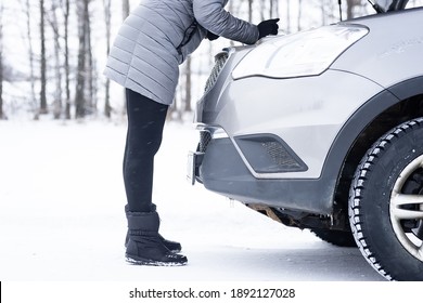 Car Repair On The Road In Winter. Young Girl Is Trying To Fix A Car Breakdown Under The Soot On The Road. Woodsroadside Assistance Car