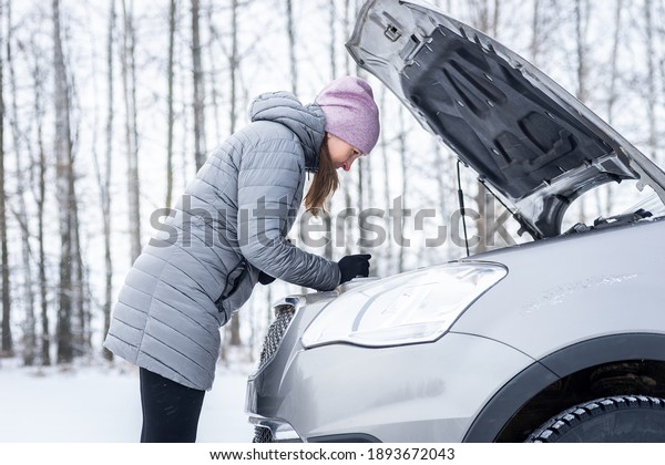 car repair on the road in winter. young girl is\
trying to fix a car breakdown under the soot on the road.\
woodsroadside assistance\
car