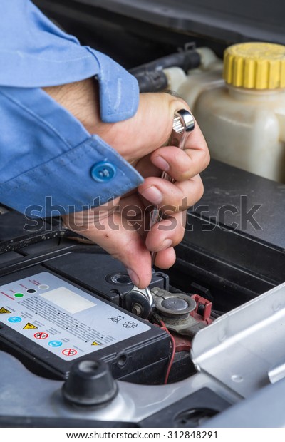 Car repair service, Auto mechanic\
checking the clamp nut of a car battery with a\
wrench