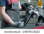 Car repair at the service center. An auto mechanic holds the front suspension lever of a passenger car in his hands. Monitoring the serviceability of the front suspension assembly.