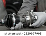 Car repair at a car service center. An auto mechanic on the desktop prepares the installation of the hub. He holds the hub and the gearbox control drive in his hands.