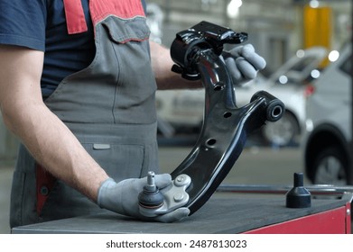 Car repair at the service center. An auto mechanic holds the front suspension lever of a passenger car in his hands. Monitoring the serviceability of the front suspension assembly. - Powered by Shutterstock