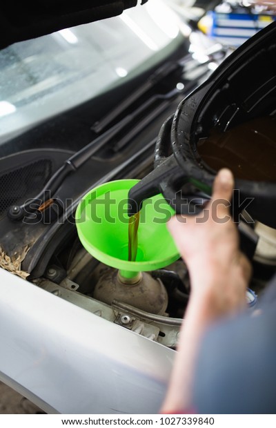 Car repair\
service center work. Mechanic man worker pouring antifreeze from\
small bottle in the cooling\
system.