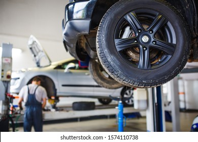Car repair in the service station. Hands of a mechanic in overalls repairing the car on the lift without wheel, holding the tire and mechanical works.