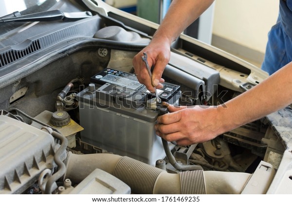 Car repair at a service station. A professional\
mechanic changes the battery on a car. The hands of a professional\
mechanic hold a tool.