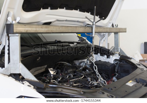 Car repair\
at a service station. A special tool is installed on the car for\
repair. The engine compartment of the\
car.