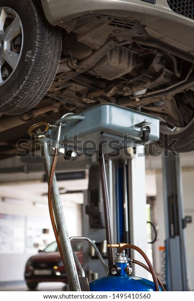 Car repair in the service station. Under the car on\
the lift substituted apparatus for draining oil and working\
off.