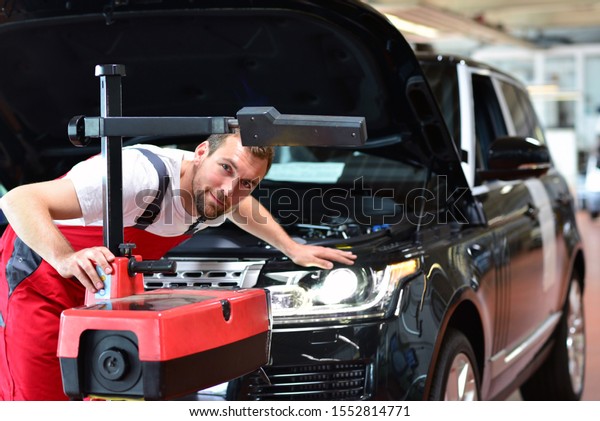 car repair shop - worker checks and\
adjusts the headlights of a car\'s lighting system \
