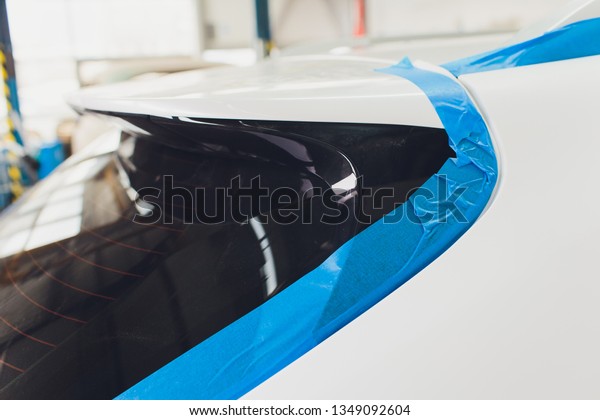 A\
car repair worker during work pastes with an adhesive tape a part\
of body element of white color in order not to fill it with paint\
during painting in a workshop on repair of\
vehicles.