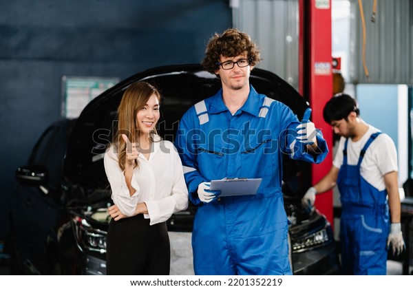  Car repairman and asian woman\
customer with checking list and repaired item at the repair garage,\
Car service and Automobile maintenance\
Concept