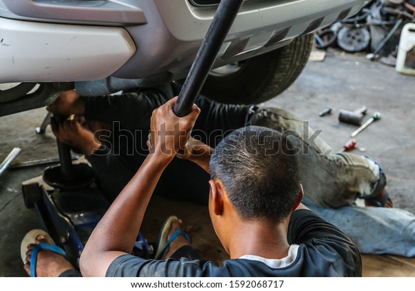   The car repairman is\
holding the iron handle, rocking the hydraulic jack, lifting the\
car, the black hand from oil stains. Jobs in car garages,\
workers.