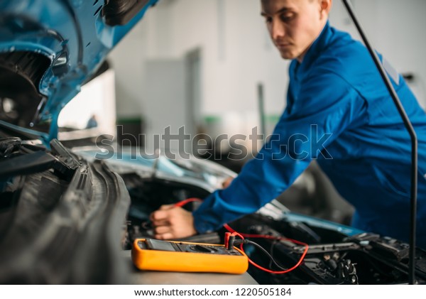Car\
repairman with multimeter, battery\
inspection