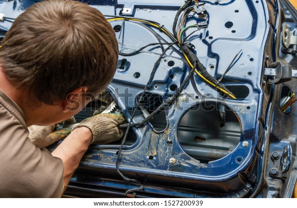 Car repairman near the disassembled car door and\
fiddling with the wires from the alarm. The concept of repair of\
the wiring of car door