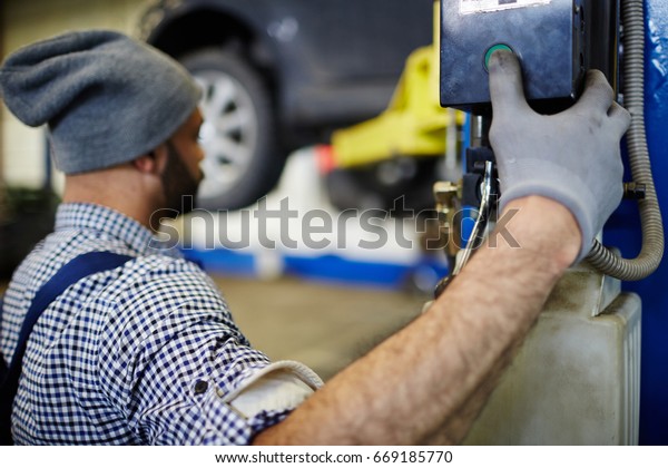 Car\
repairman pressing button to descend\
machine