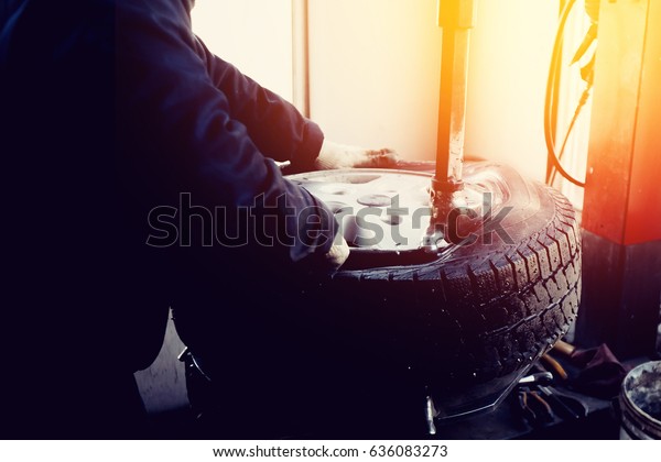 car repairman\
repairs the rubber tire from the car wheel on the balance machine\
apparatus in the workshop.\
Blick.