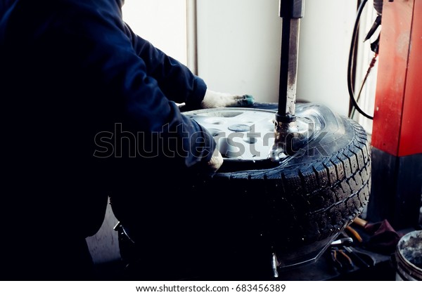 car repairman repairs\
the rubber tire from the car wheel on the balance machine apparatus\
in the workshop.