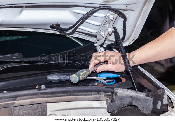 A car\
repairman unscrews parts with a wrench with a green handle in the\
engine compartment in a vehicle repair\
workshop