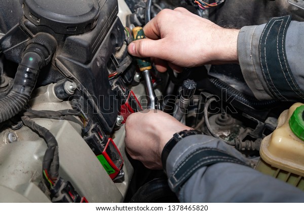 A car\
repairman unscrews parts with a wrench with a green handle in the\
engine compartment suh as spark plugs and ignition coils in a\
vehicle repair workshop. Auto service\
industry.
